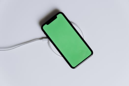 Home A minimalist smartphone with a green screen on a wireless charger, ideal for tech mockups.
