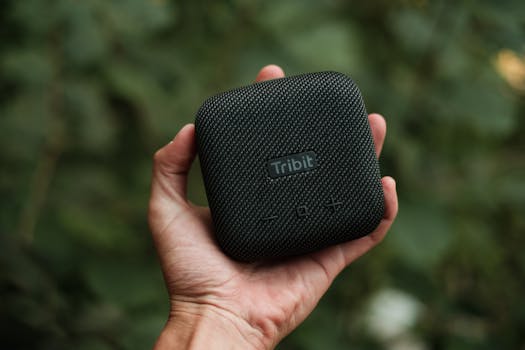 Home Crop unrecognizable person demonstrating contemporary square shaped portable loudspeaker near trees in daylight